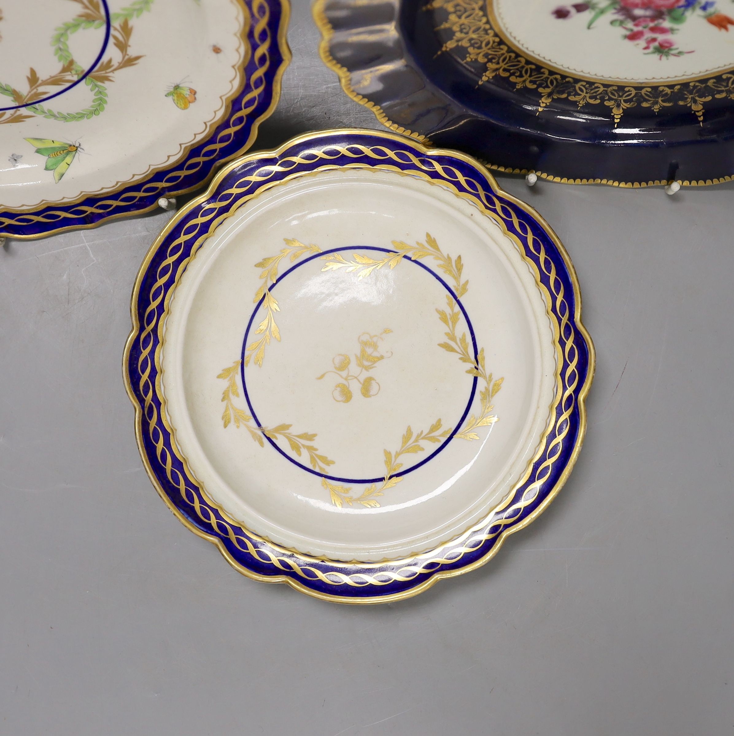 Three Worcester plates having blue border, one with elaborated gilding enclosing a bouquet of flowers, two plates both with a star shaped foliate design in the centre, c.1775, largest 21.5 cm